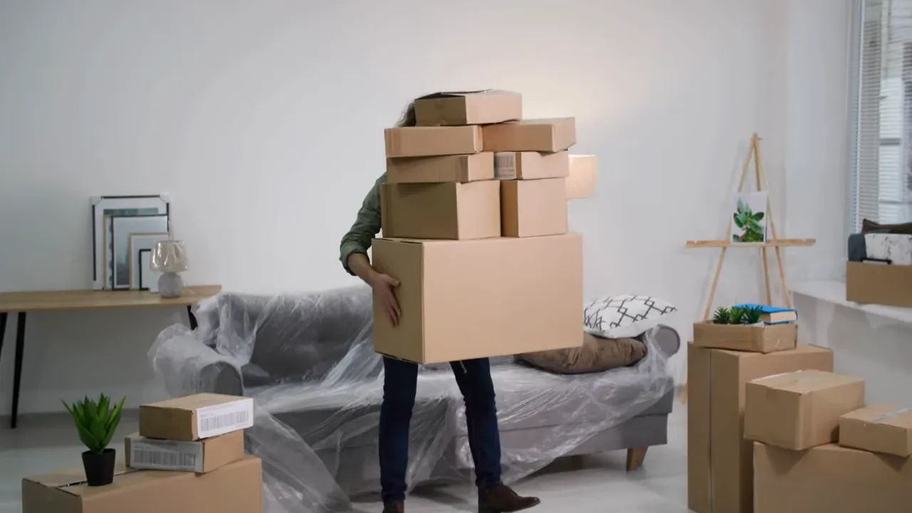 Person carrying stacked moving boxes in a living room