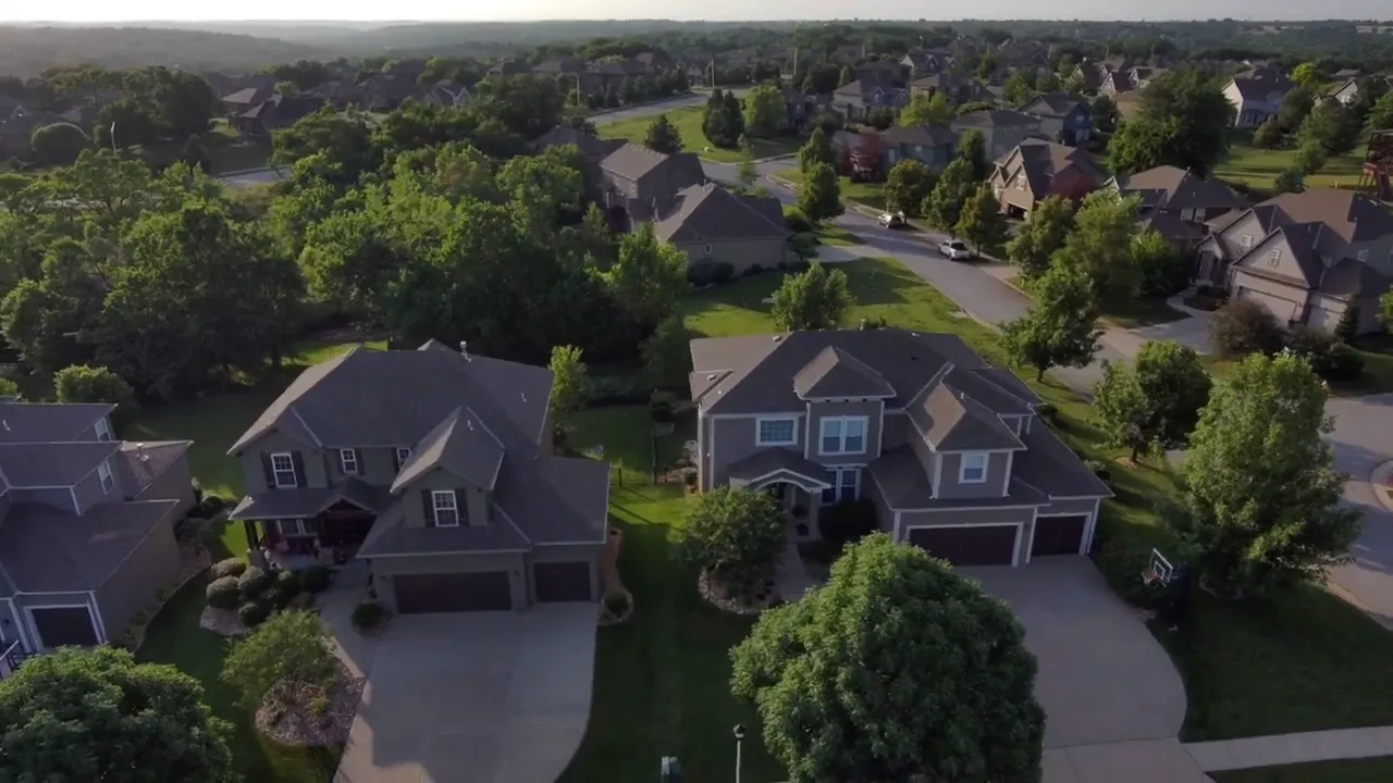 High-angle aerial photo of suburban houses, driveways and tree-lined streets showing a neighborhood layout