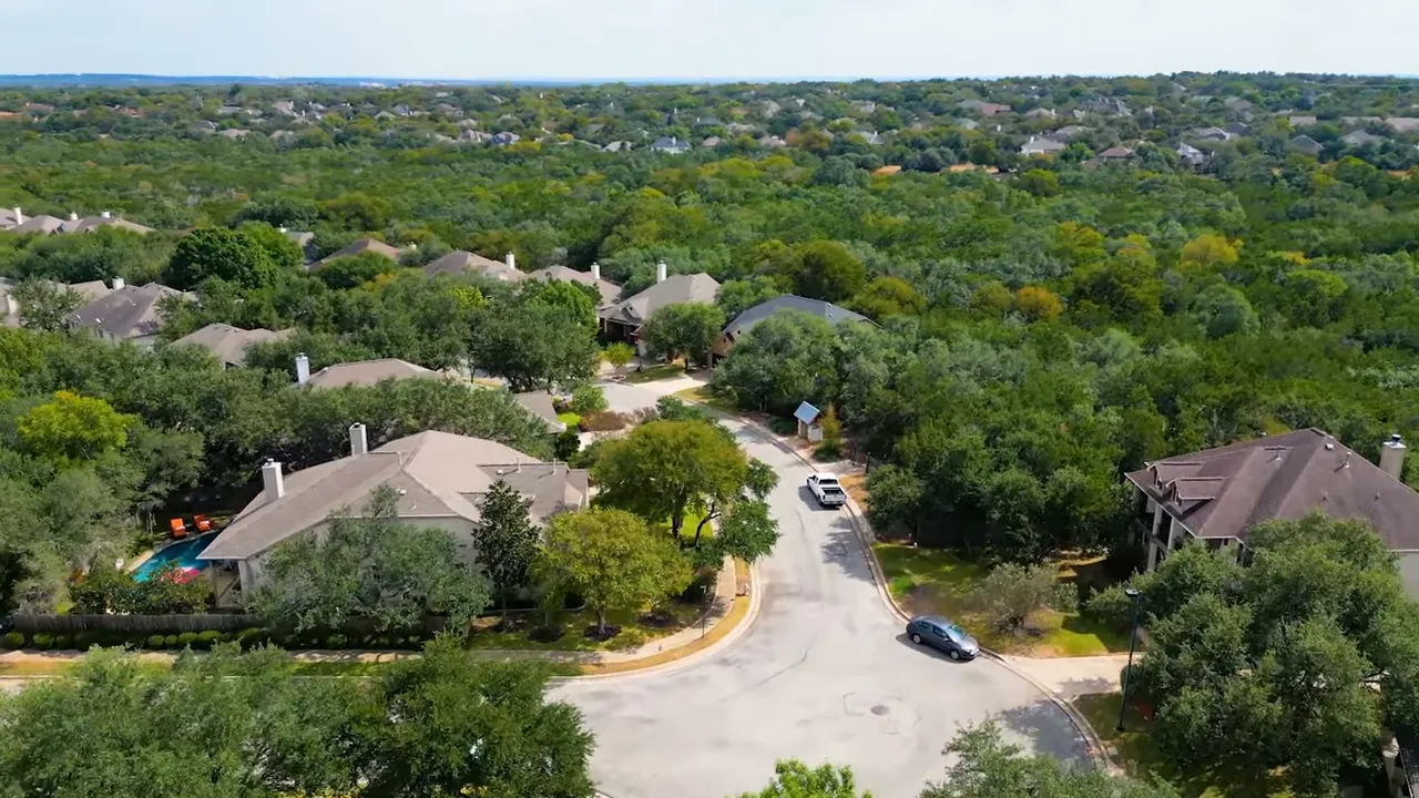 Wide aerial view of a residential cul-de-sac in Austin with houses, trees, a visible backyard pool and neighborhood streets.