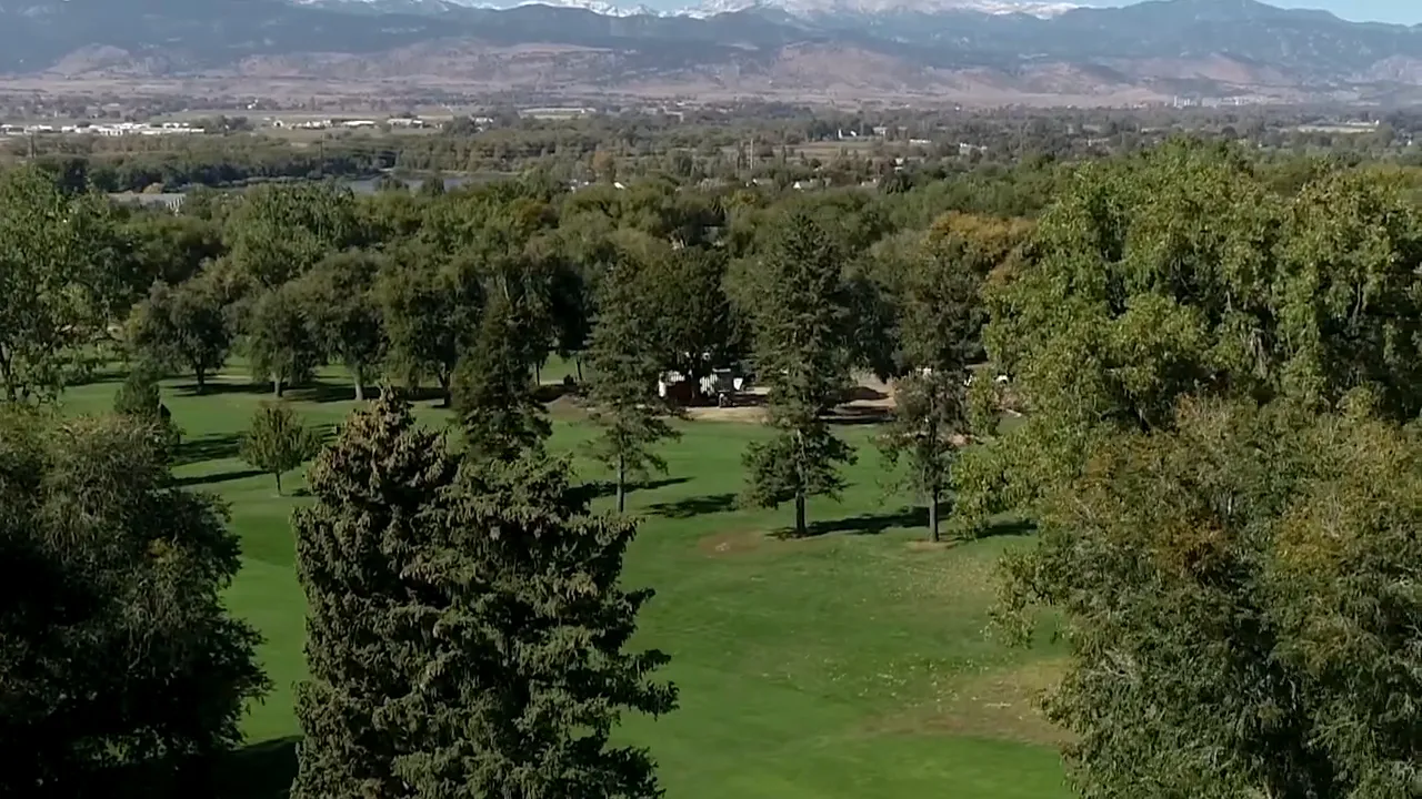 View of Longmont Colorado green spaces and neighborhood rooftops with mountain range in the distance