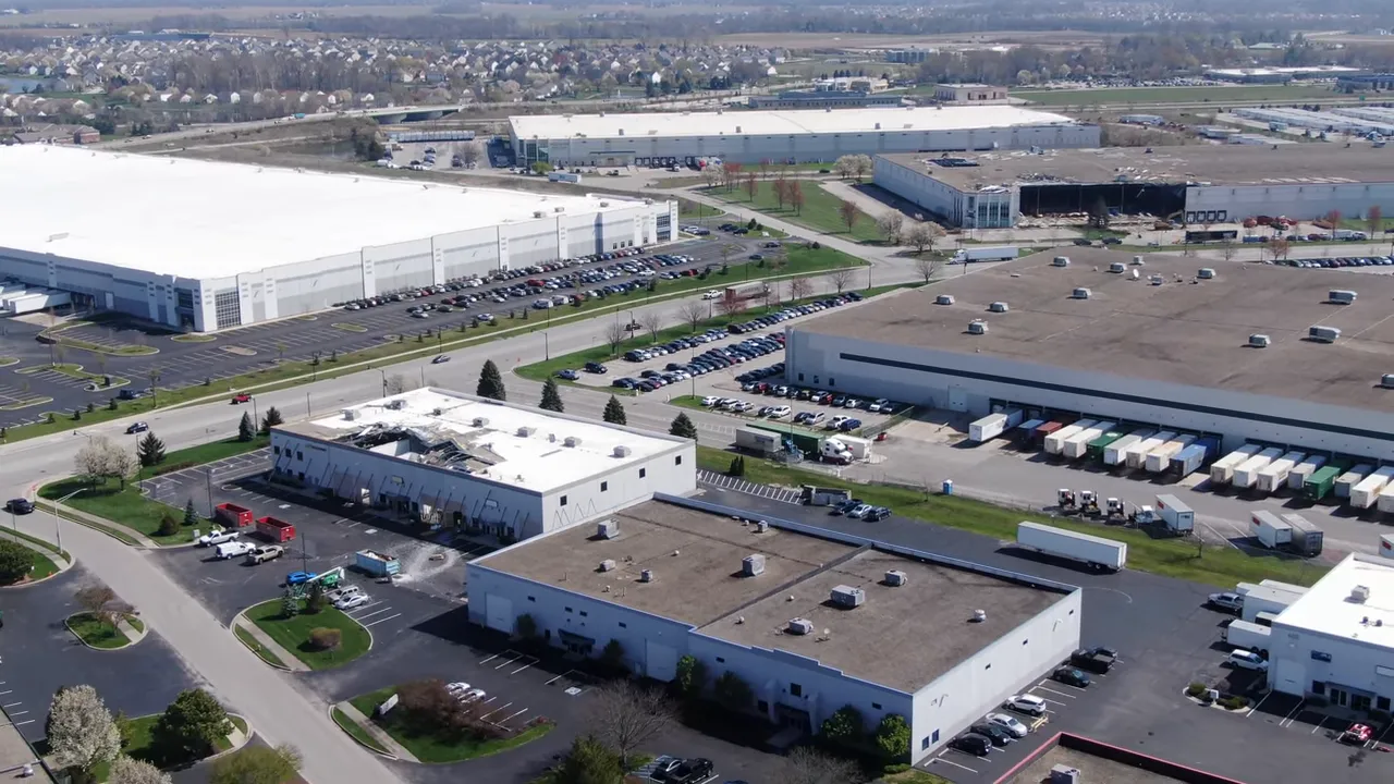 Aerial drone view of an industrial park in Brownsburg with one warehouse that has a large section ripped away and surrounding intact buildings and parking lots.