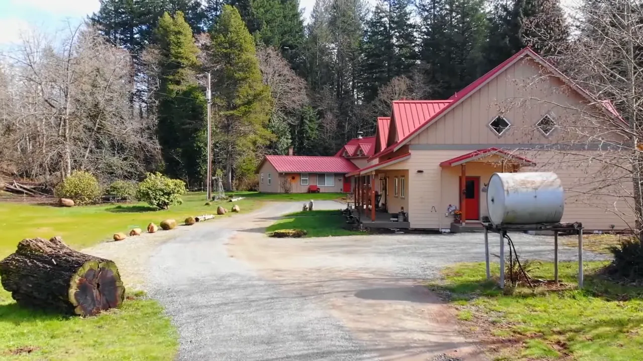 Rural home with red roof long driveway and propane tank near the garage
