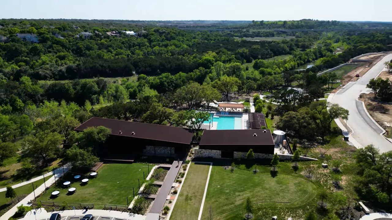Aerial view of a neighborhood clubhouse with pool, lawns, parking and surrounding trees