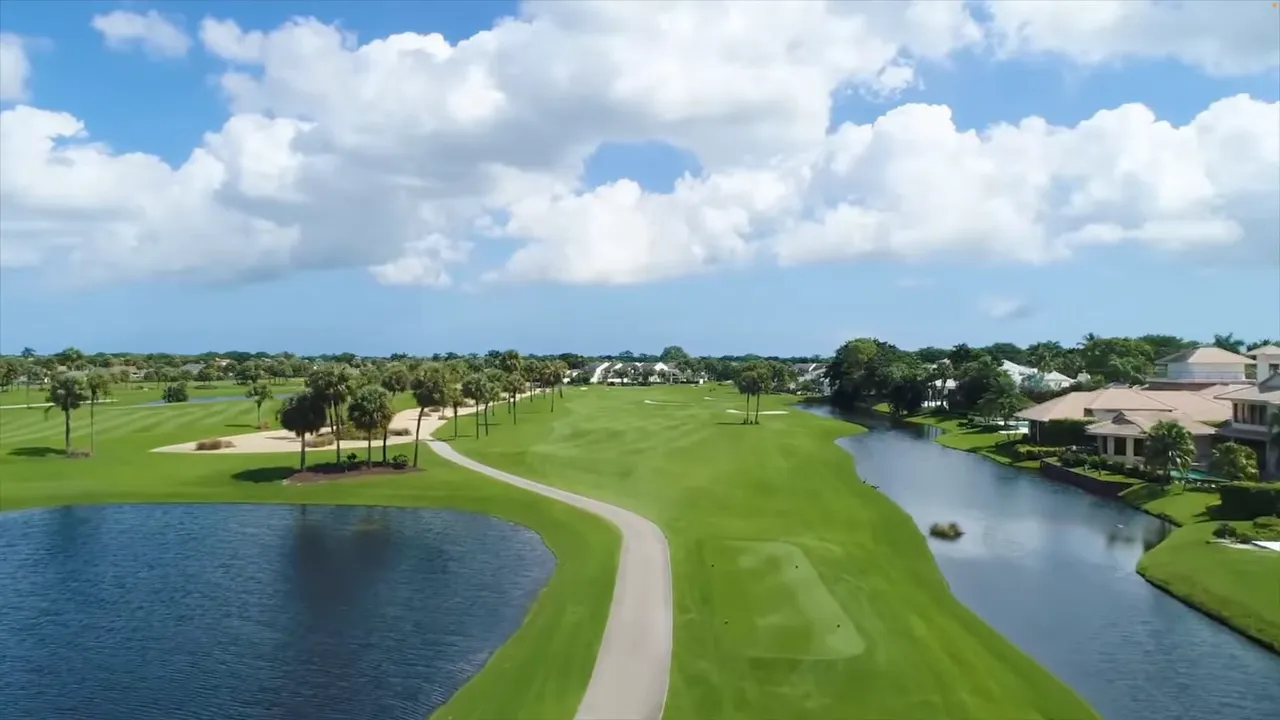 Aerial view of a long golf fairway with water hazards, bunkers, palm trees, and homes at Boca West.