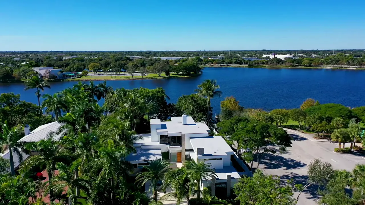 Aerial view of a luxury waterfront Delray Beach estate with tree-lined lot and large lake in the background