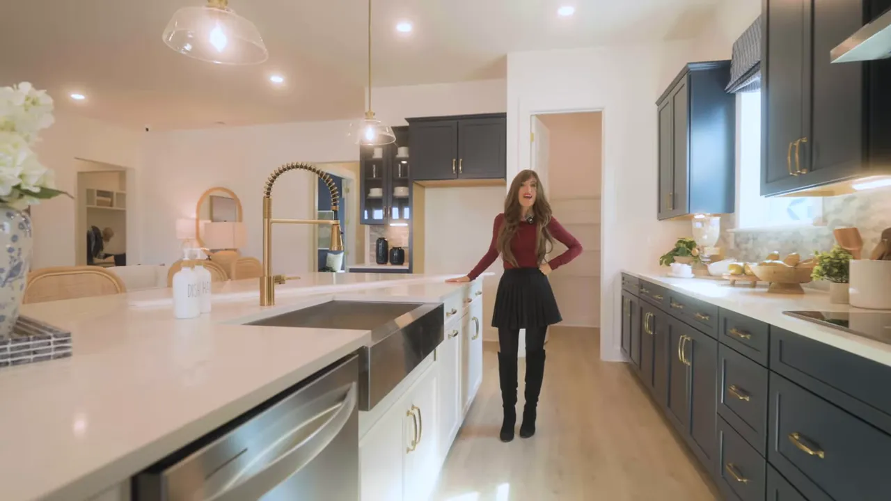 Open-concept kitchen with oversized white island, gold faucet, pendant lights and dark shaker cabinets