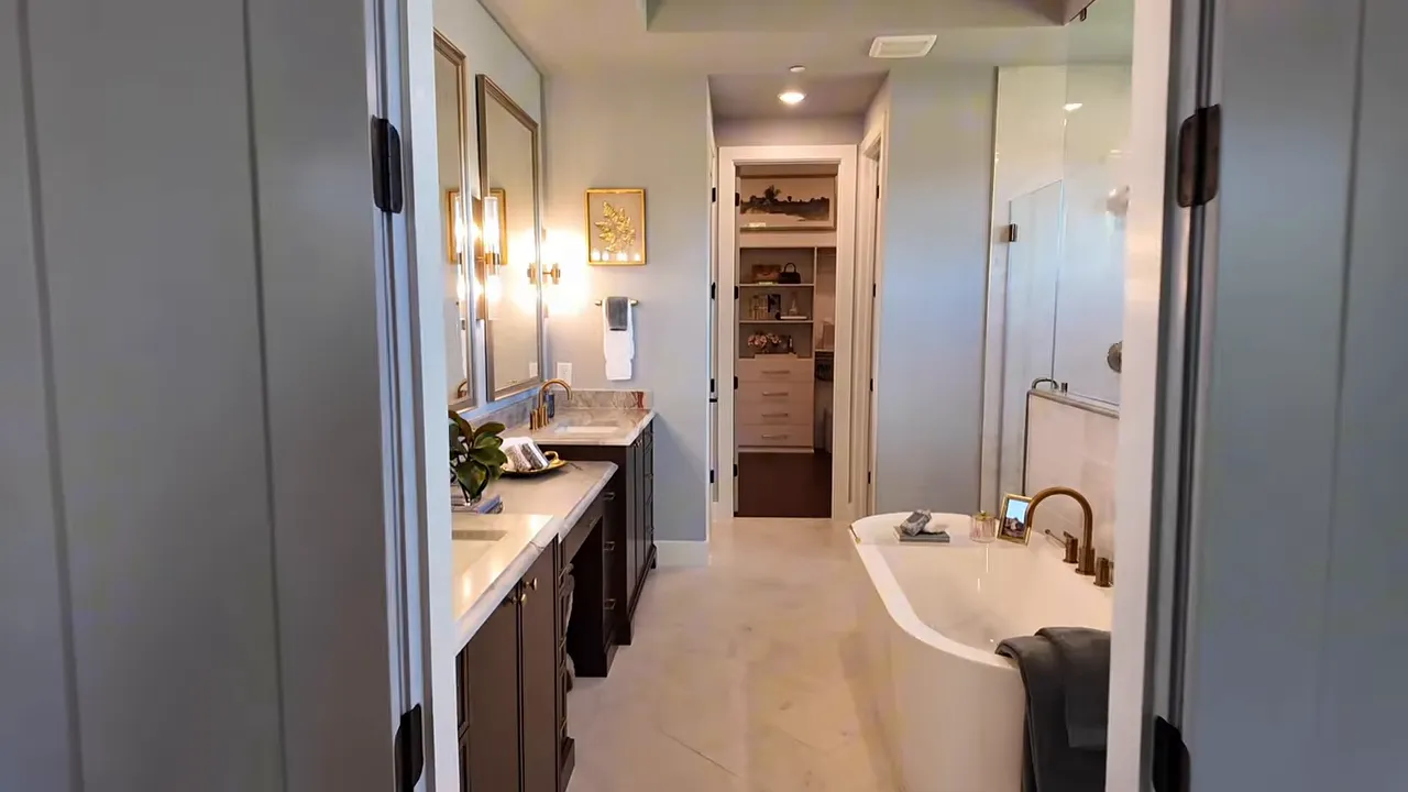 Luxury primary suite bathroom with dual sink vanity, gold fixtures, and a walk-in closet view