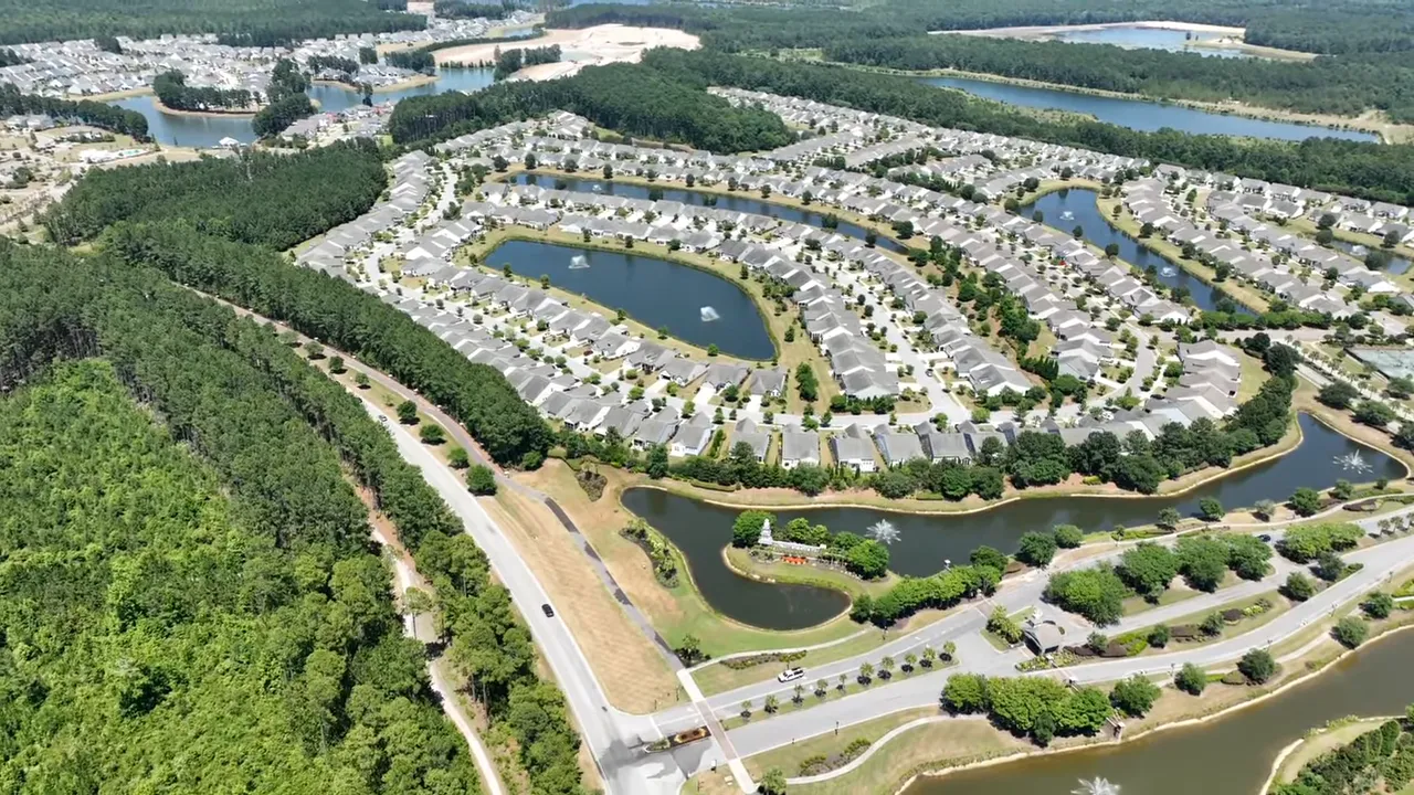 Aerial view of a suburban neighborhood with curved streets, ponds, green buffers and clustered single‑family homes.