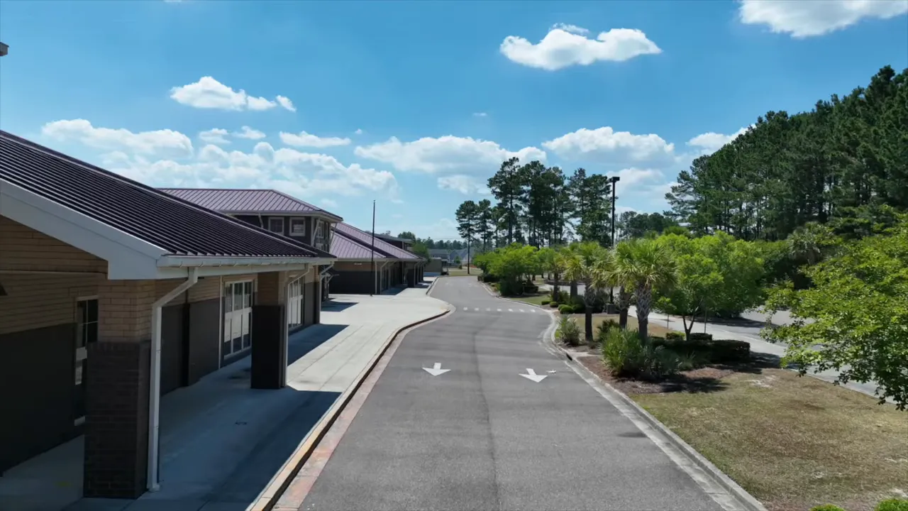 Aerial view of a school's drop-off lane, sidewalks, palm trees and adjacent parking area under a clear blue sky.