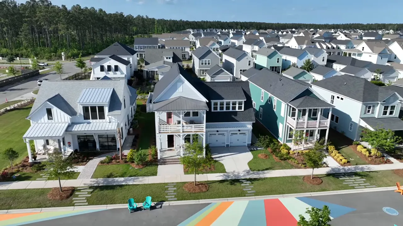 Wide aerial of a row of modern homes with sidewalks and a painted community street area showing neighborhood scale and walkability