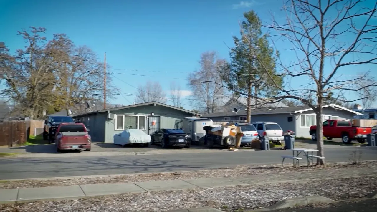 Residential neighborhood street with multiple parked vehicles and clutter near neighboring properties