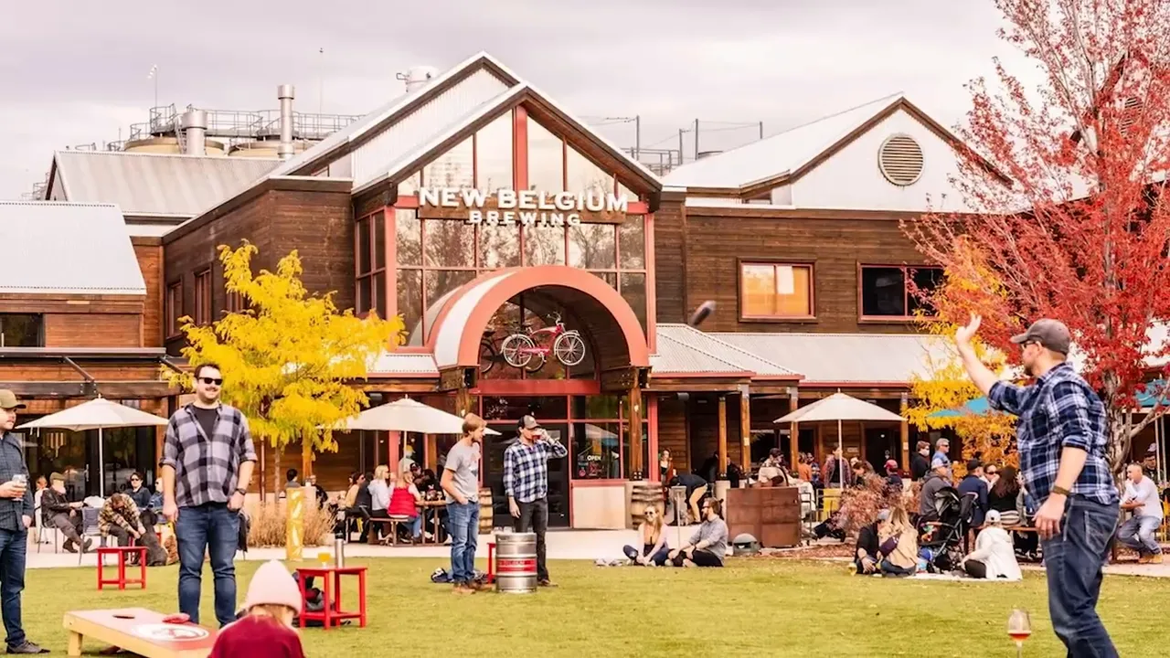 People gathered on a lawn outside a brewery building playing yard games