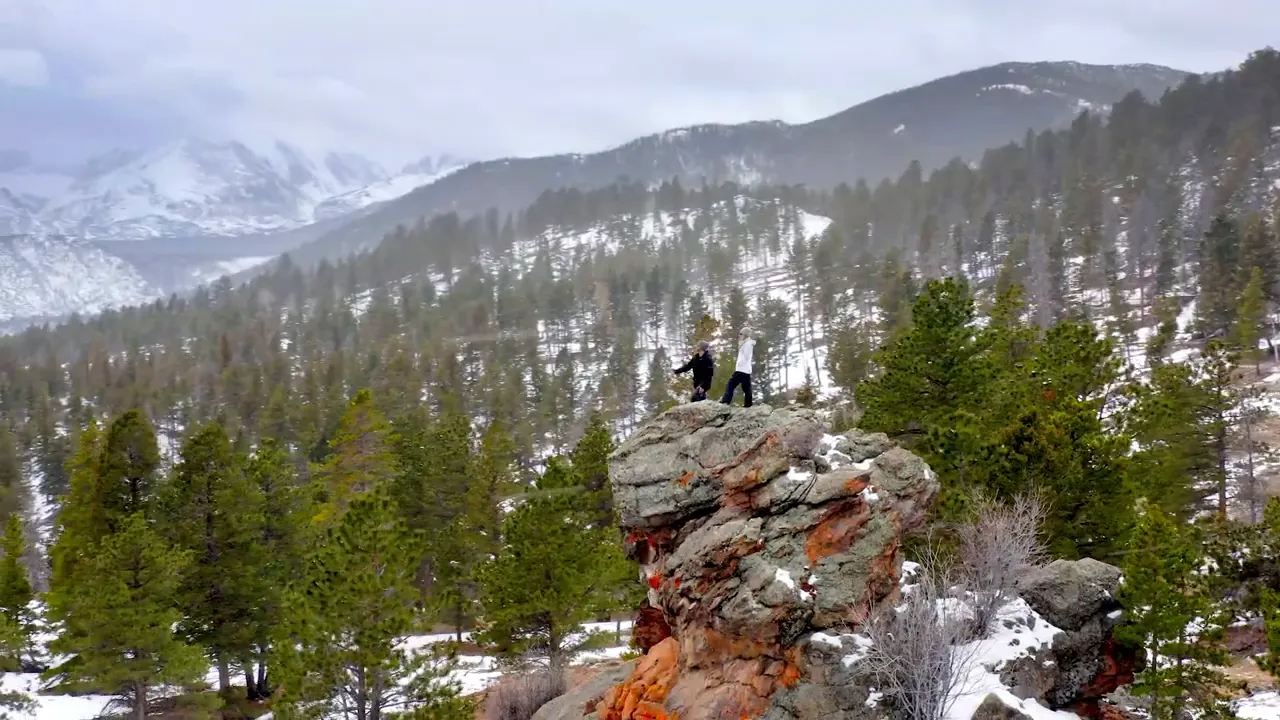 Snowy mountain landscape with two people standing on a rocky outcrop