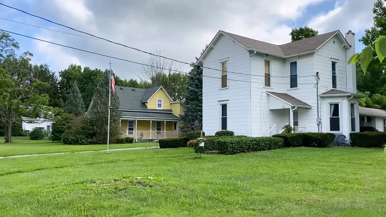 Historic white two story home with a covered porch large tree and landscaped front yard