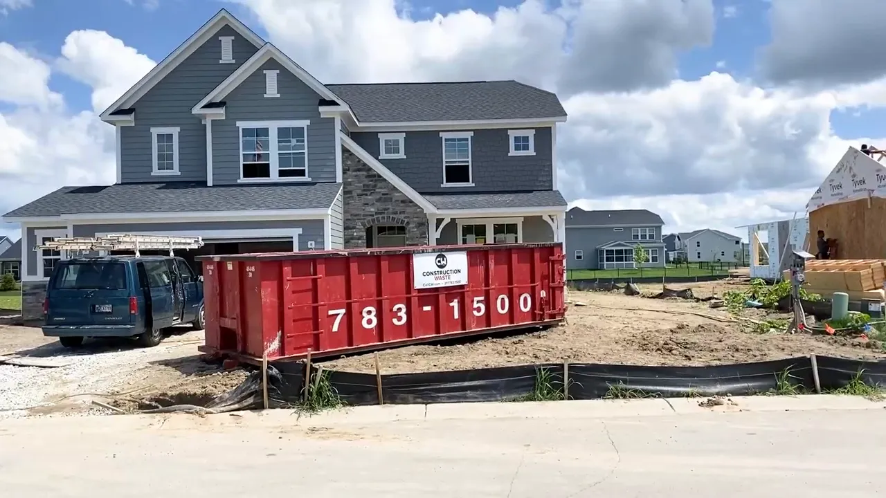New two story house under construction beside a large red construction dumpster
