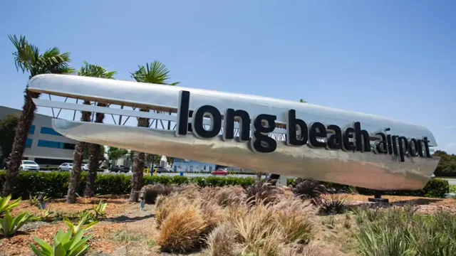 Long Beach Airport sign beside landscaped plants under blue sky
