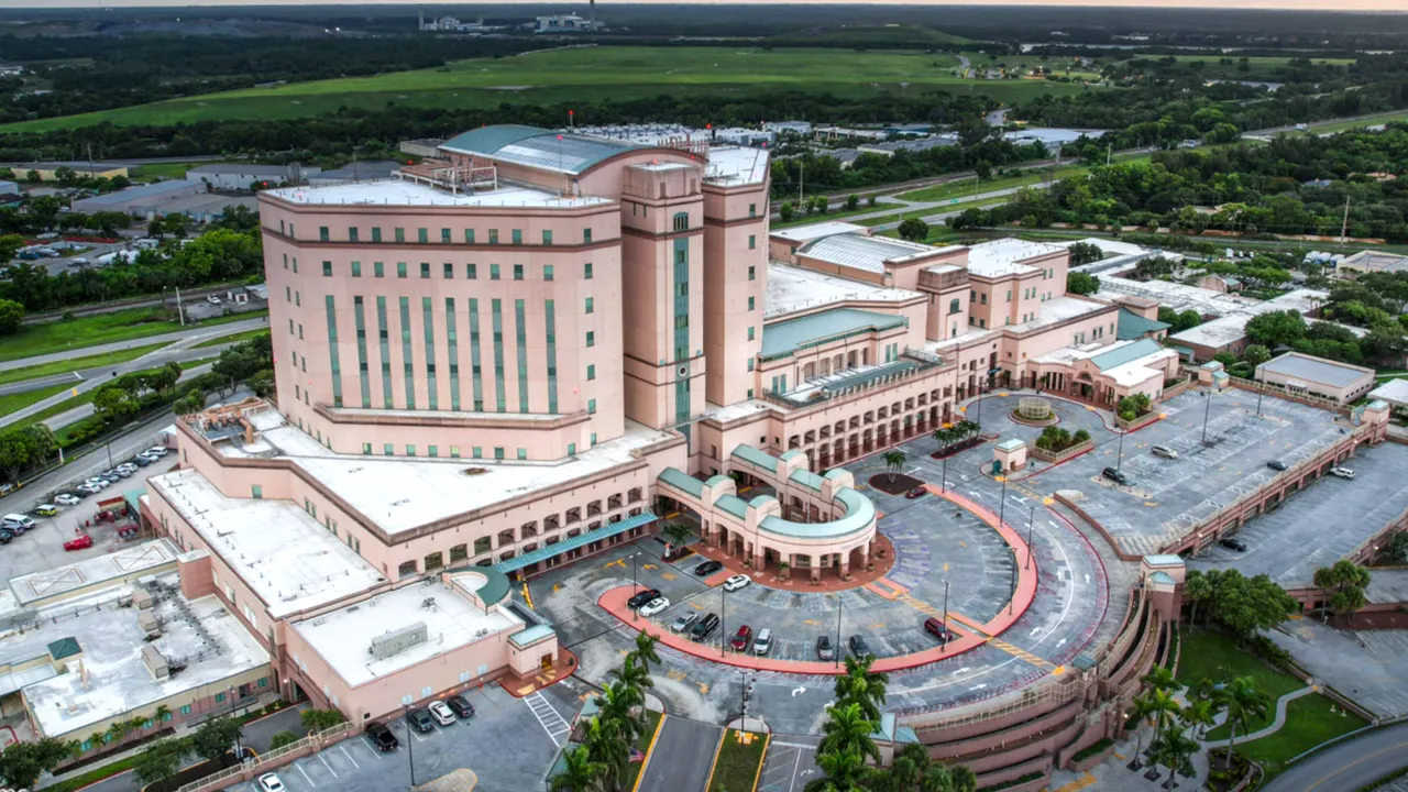 Aerial view of a large hospital complex with a circular main entrance, parking areas, and surrounding greenery.