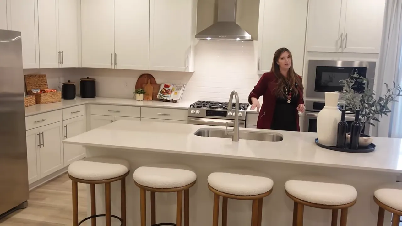 White kitchen with large island stools gas range and stainless refrigerator