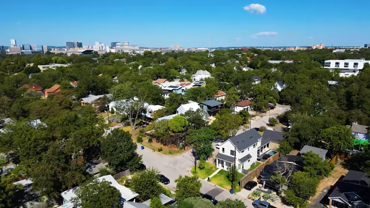 Wide drone panorama of an East Austin neighborhood with houses, many trees and the downtown skyline on the horizon
