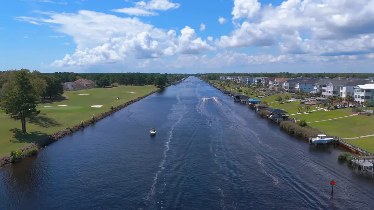 Canal view with boats, waterfront homes, and a golf course under a blue sky near Myrtle Beach.