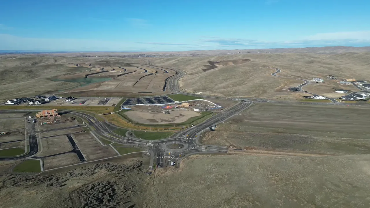 High-resolution drone aerial of a master planned community showing roundabout, central recreation area, lot layouts and rolling foothills.