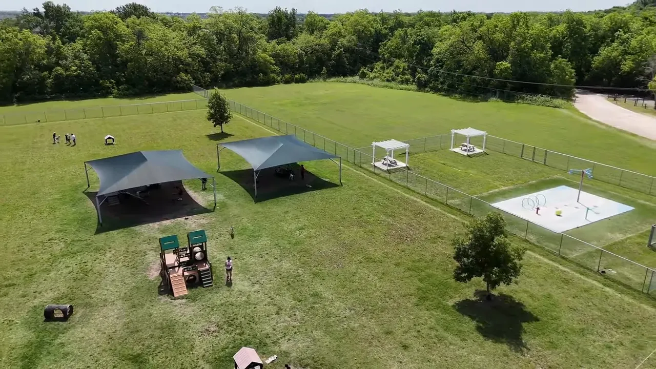 Aerial view of Hutto dog park with multiple shaded play areas, fencing, and open lawn space