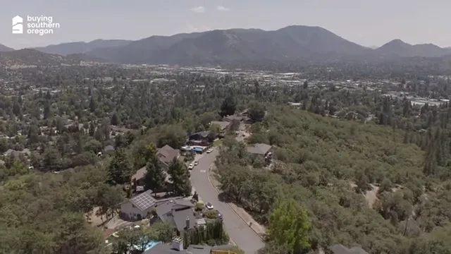Aerial view of homes along a wooded ridge overlooking Grants Pass and surrounding mountains