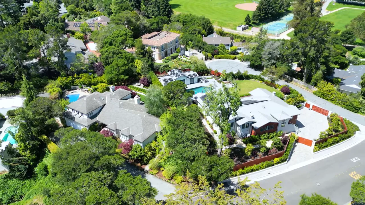 Clear aerial view of a cul-de-sac with multiple houses, landscaped yards, swimming pools and a park visible beyond