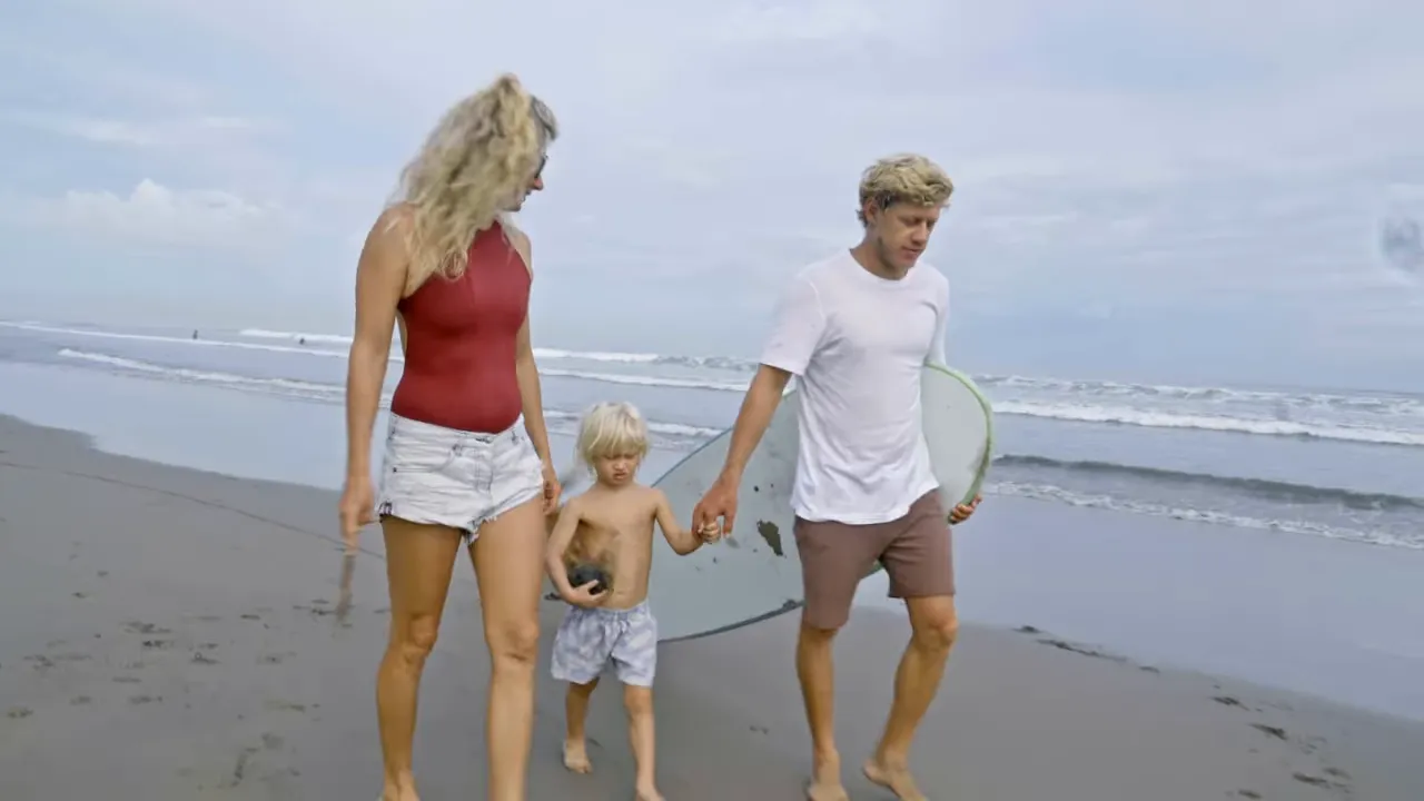 Video screenshot of a family walking on the beach with a surfboard