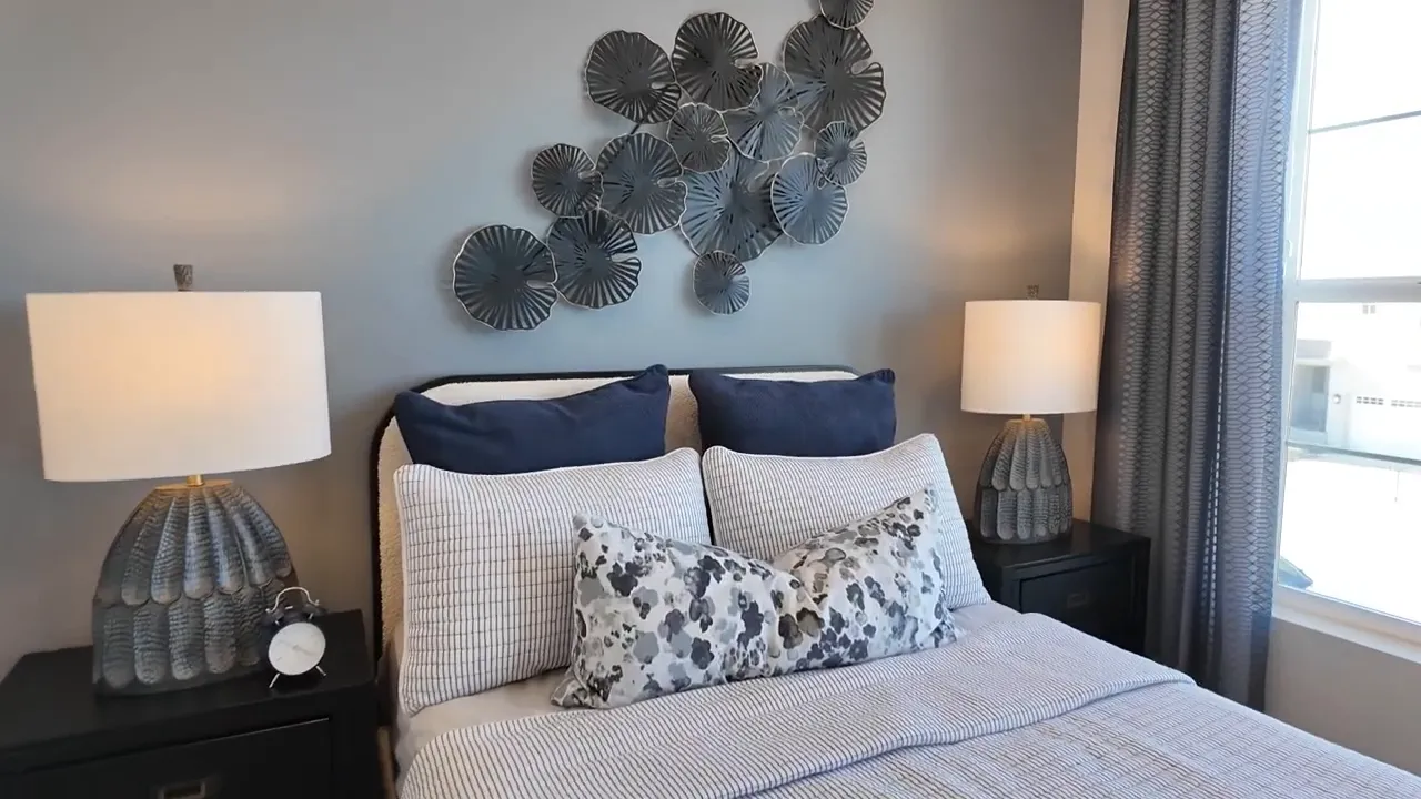 Wide view of staged primary bedroom in Tri Pointe Aurora Highlands with bed, lamps, and window light