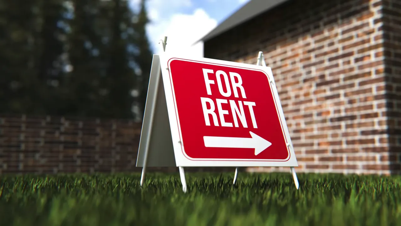 Red and white for rent sign in grass near a brick building