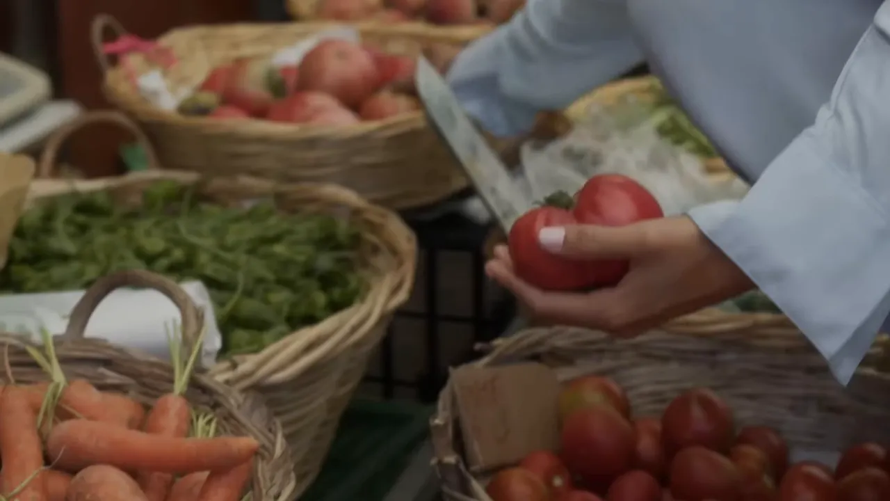 Market table with baskets of produce and hands holding large tomatoes