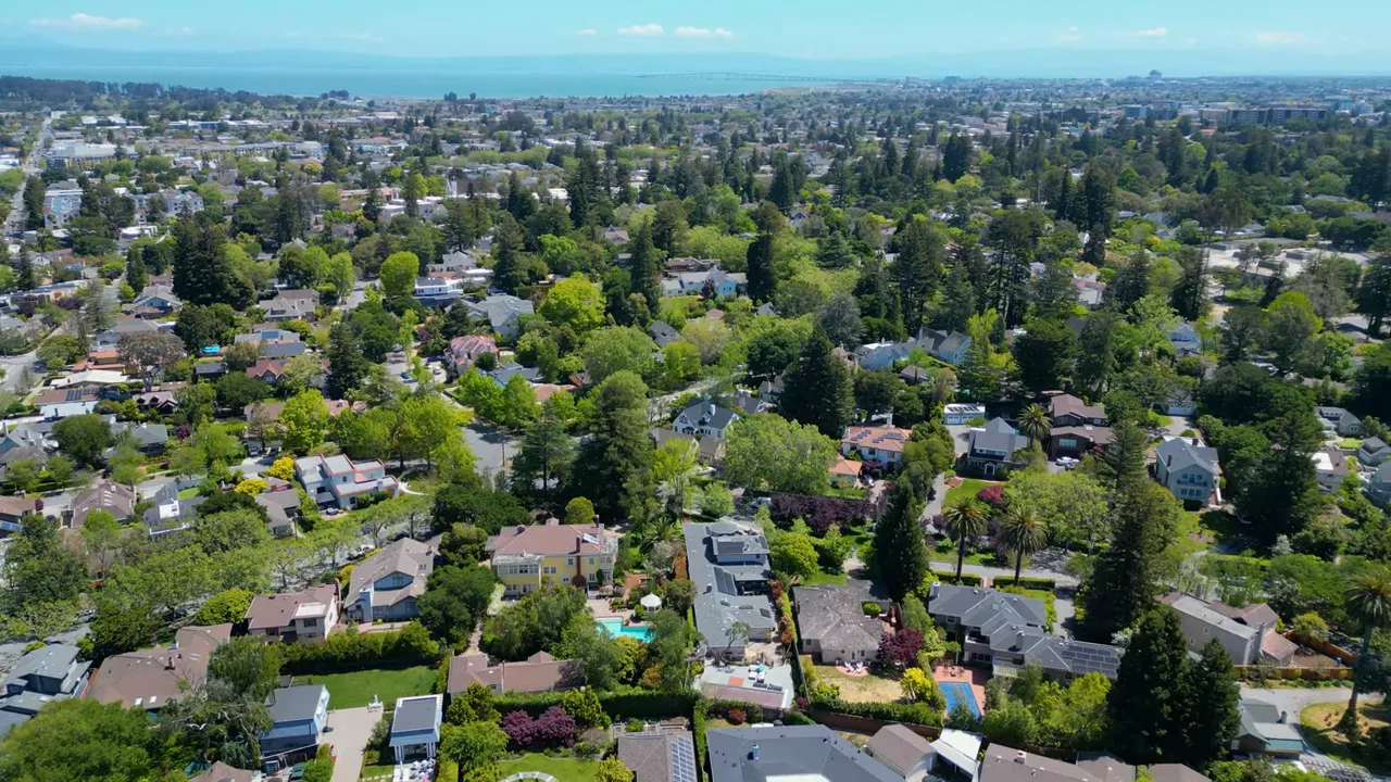 Drone aerial of Burlingame neighborhoods with dense tree canopy and San Francisco Bay visible on the horizon