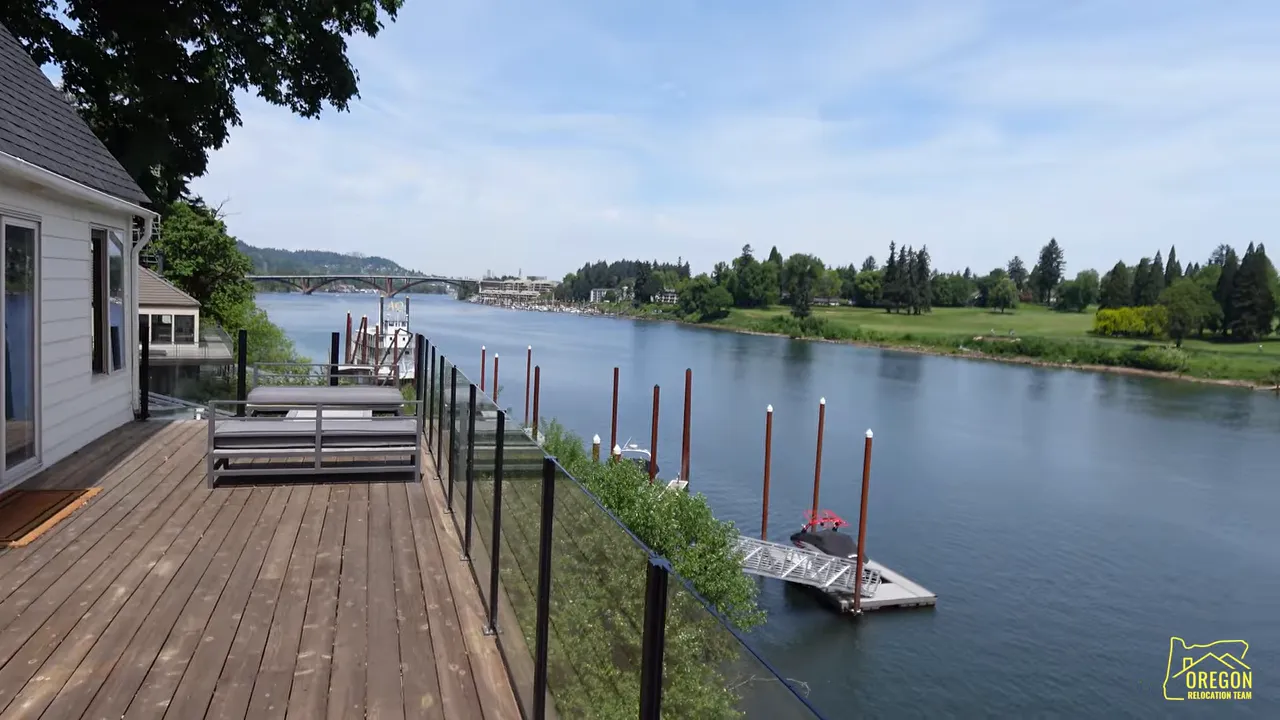 Wood deck running along riverfront with glass railing and dock below