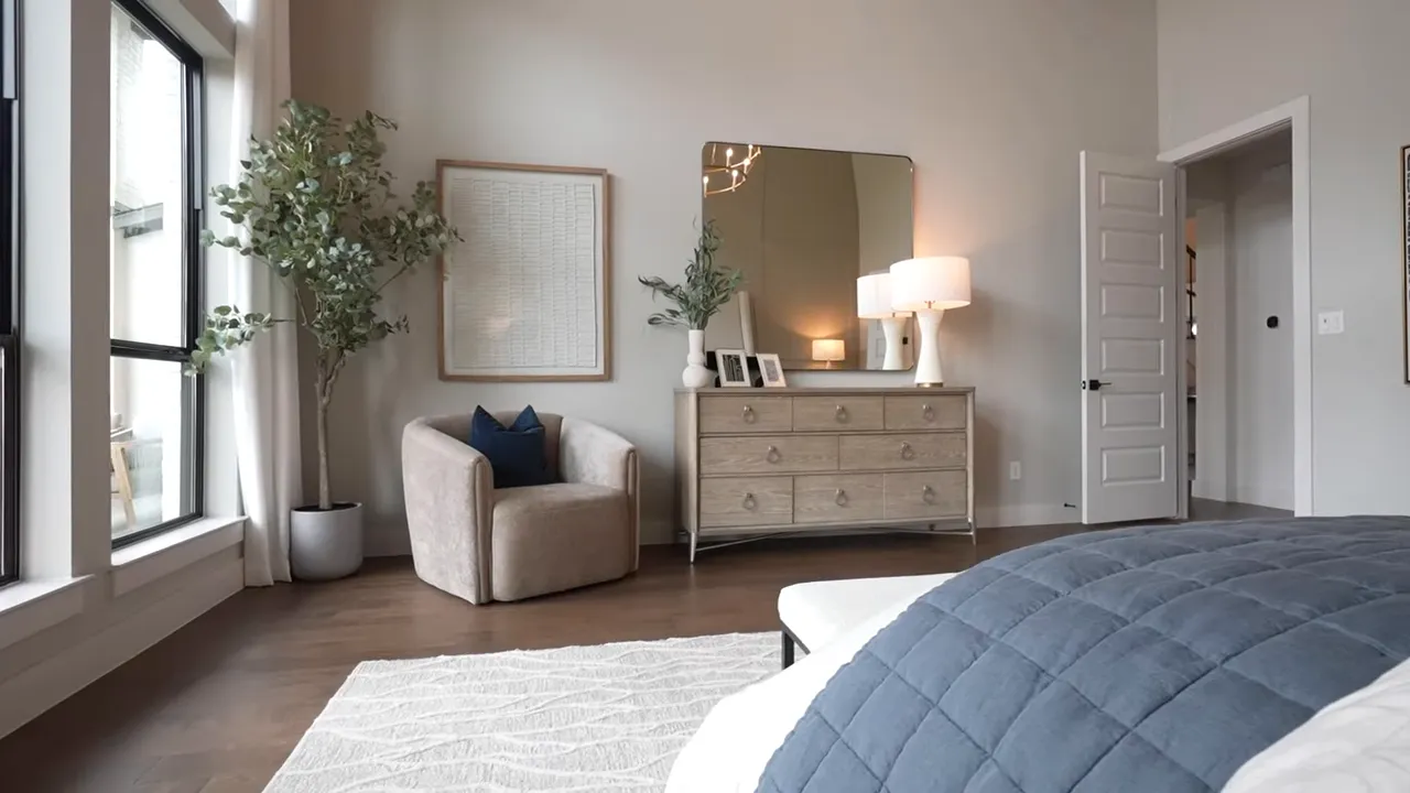 Spacious primary bedroom with seating area, dresser, and large windows