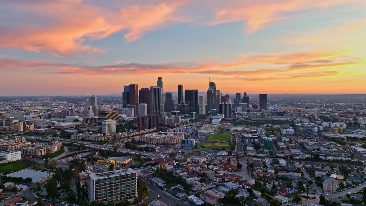 Aerial neighborhood and city skyline at sunset showing residential streets and buildings.