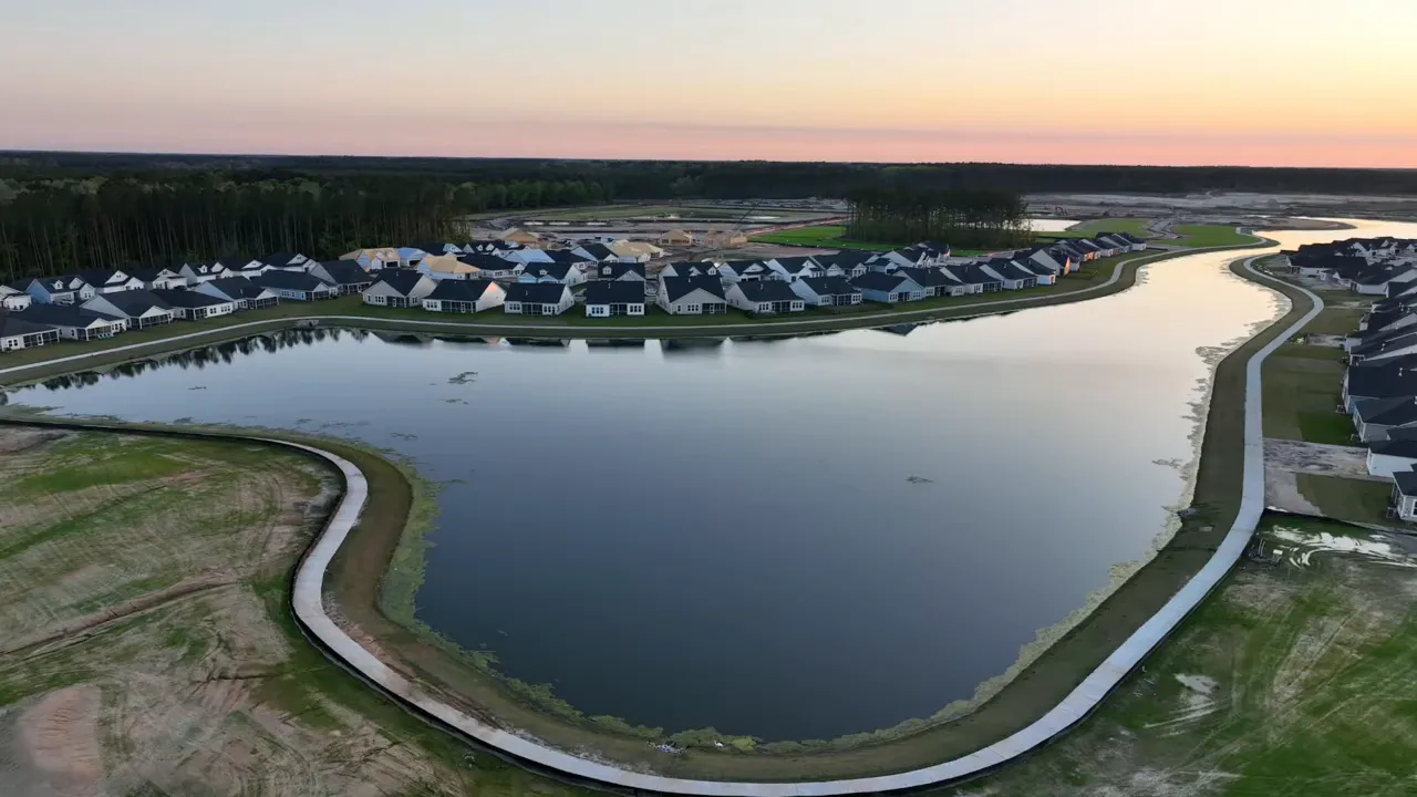 Drone view of a residential community lake and curving road along the water at sunset