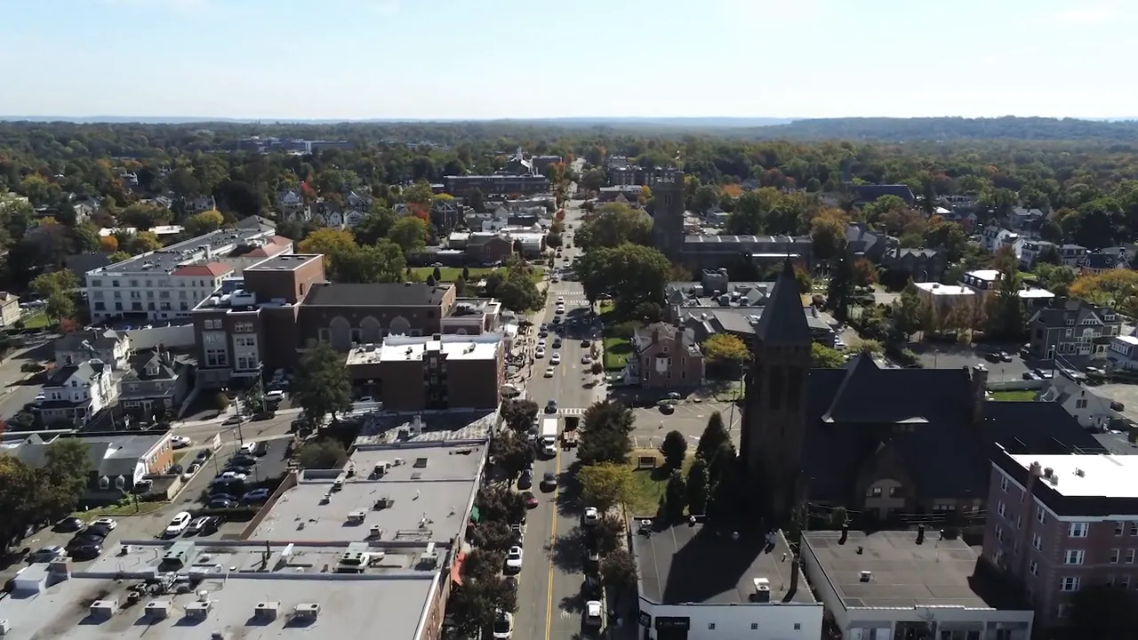 Wide aerial view of a small town, surrounding trees, and rolling hills in the distance