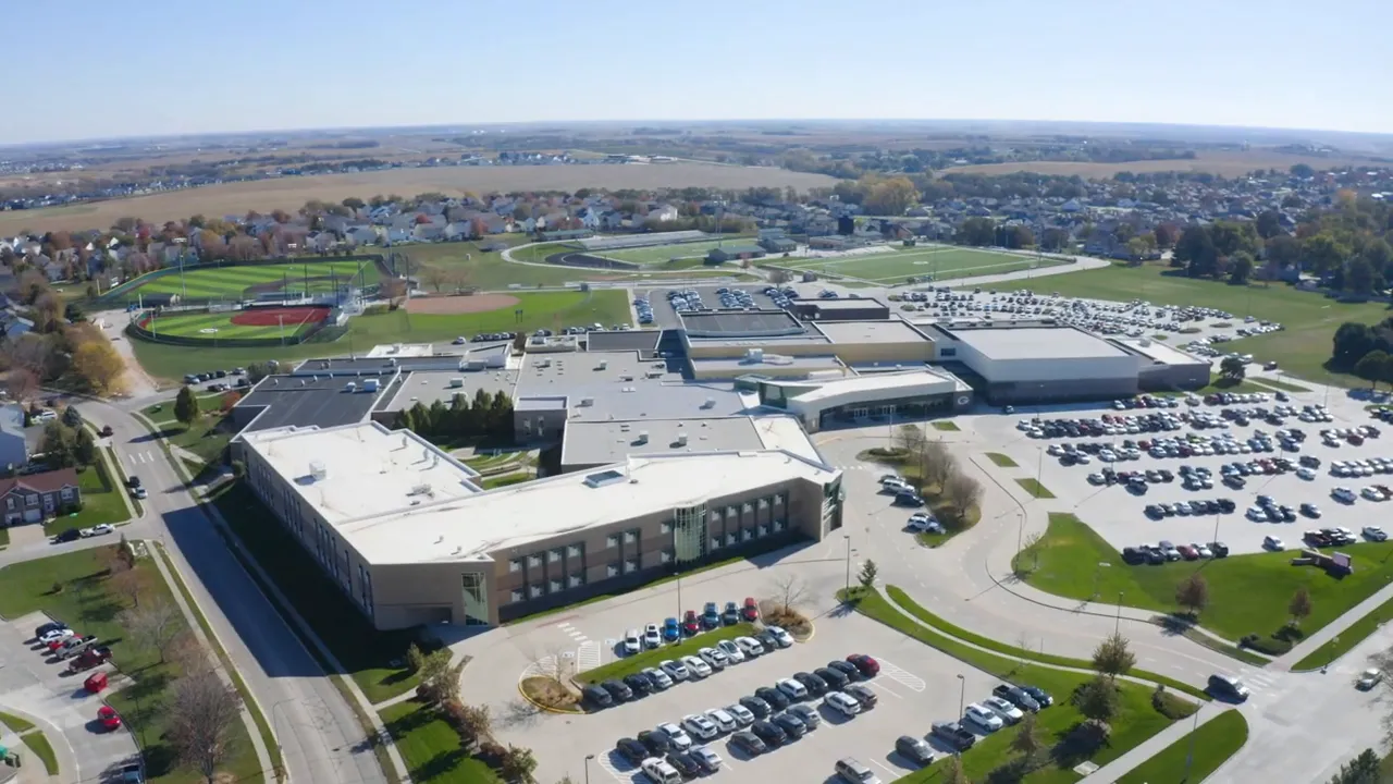 High-resolution drone aerial of a suburban high school campus with multiple buildings, athletic fields and parking lots