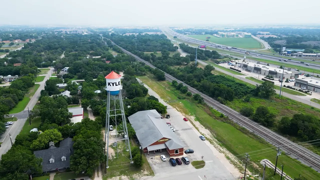 Wide aerial shot of Kyle with the water tower, nearby railroad tracks, and a highway corridor visible