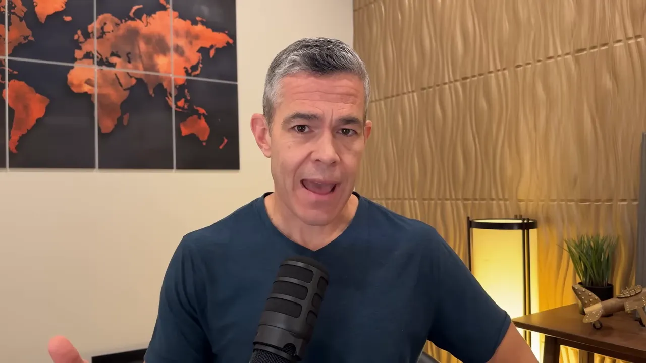 Presenter gesturing in a home studio with a world-map artwork, microphone and desk lamp visible.