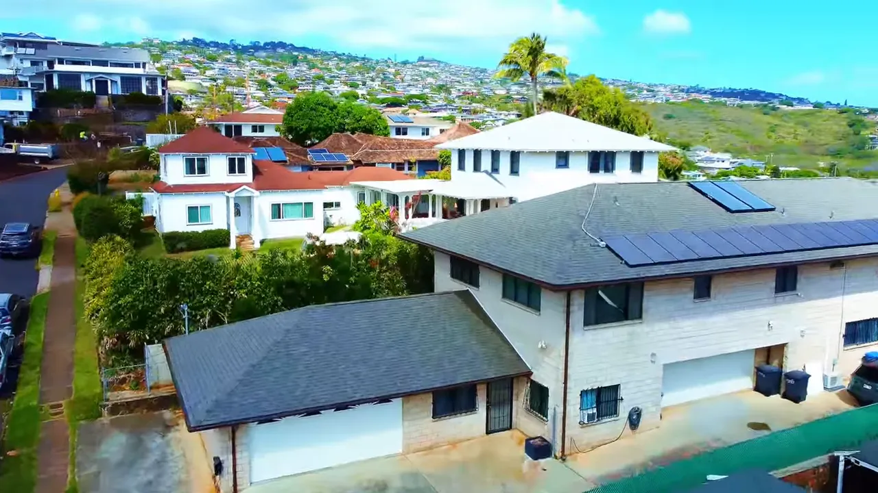 Aerial view of single-family homes and rooftops in a residential neighborhood, showing solar panels and street layout.