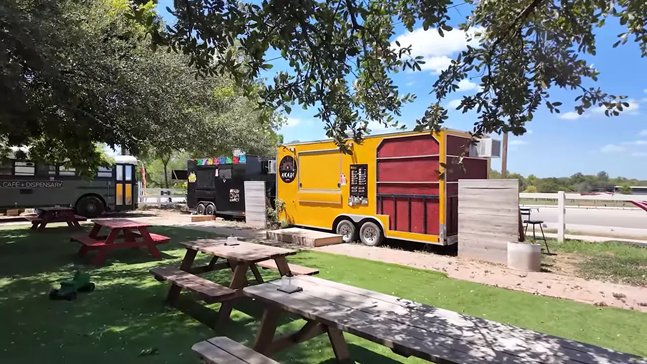 Colorful food trailers beside picnic tables under large trees