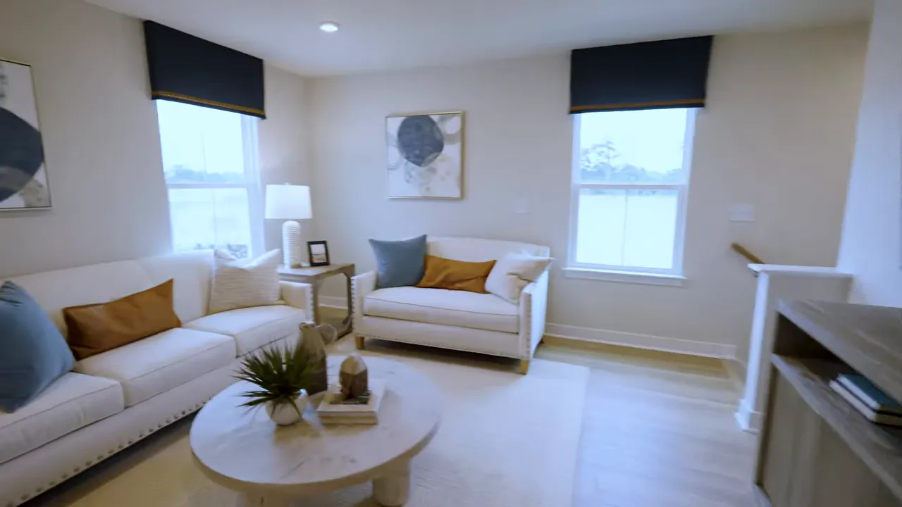 Open living room with white sectional, blue pillows, round coffee table, and large windows