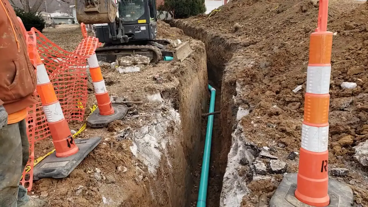 open trench with exposed sewer pipe and orange traffic cones during repair work