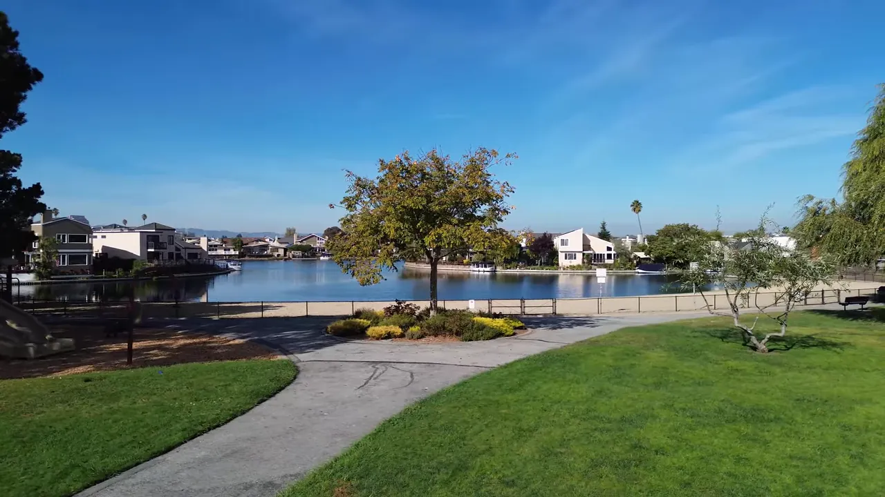 Foster City lagoon with park pathway, grassy lawn, and waterfront homes under a blue sky