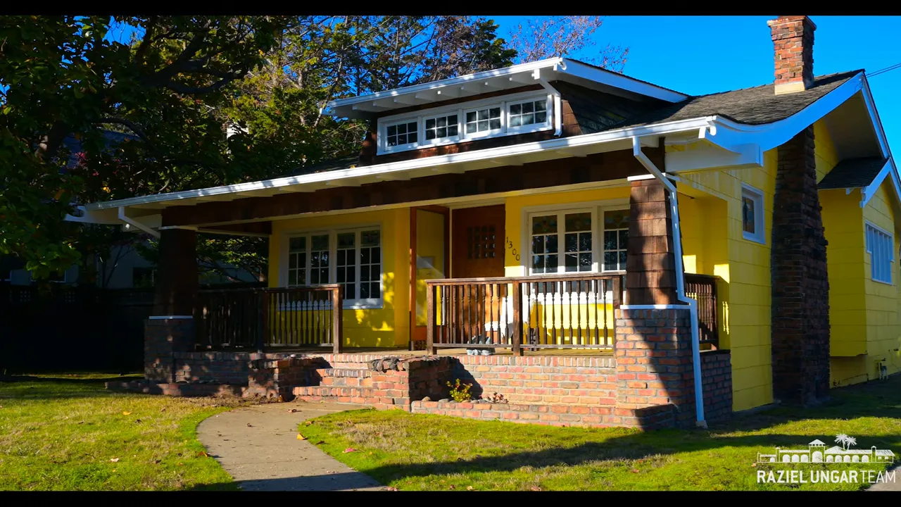Wide view of a yellow Craftsman bungalow showing front yard, brick porch and lot size