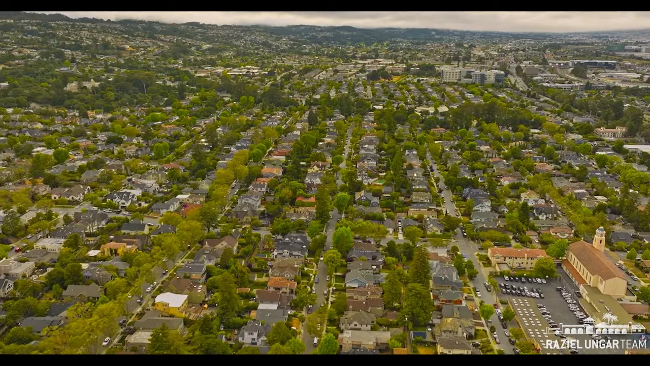 Wide aerial shot of Burlingame neighborhoods, tree-lined streets, and commercial area in the distance.