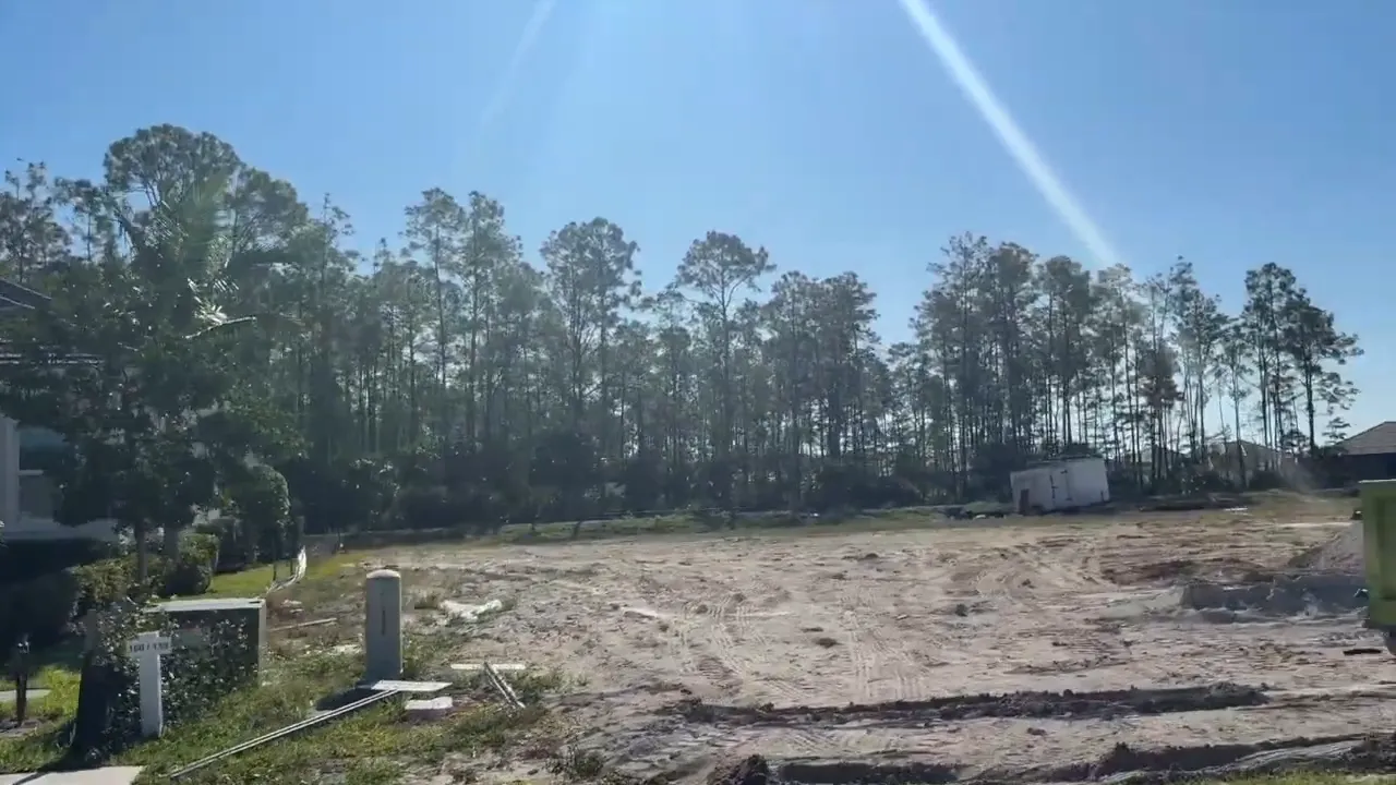 Open construction lot with sandy ground trees and a large green dumpster