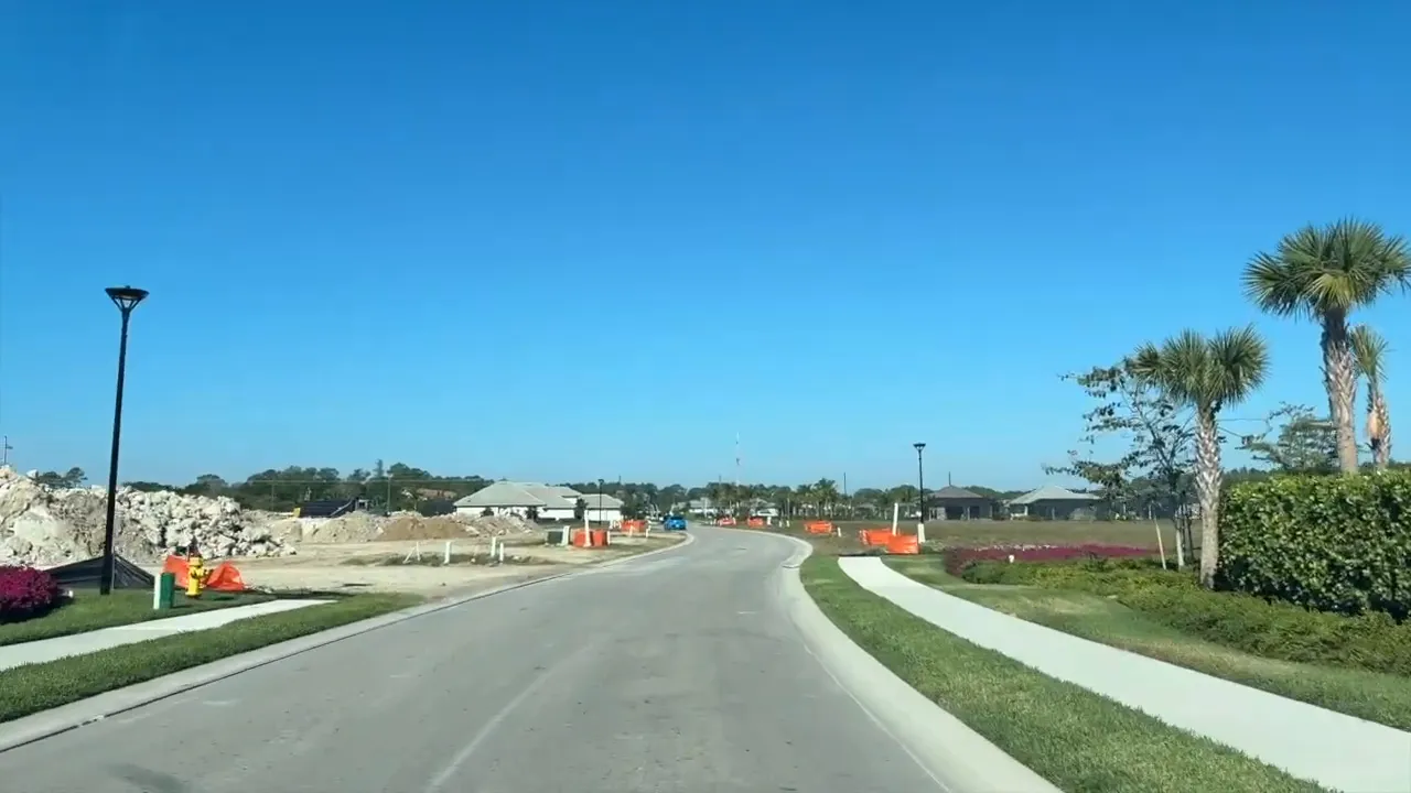 Newly paved road through active construction area with orange safety barriers and landscaped sidewalk